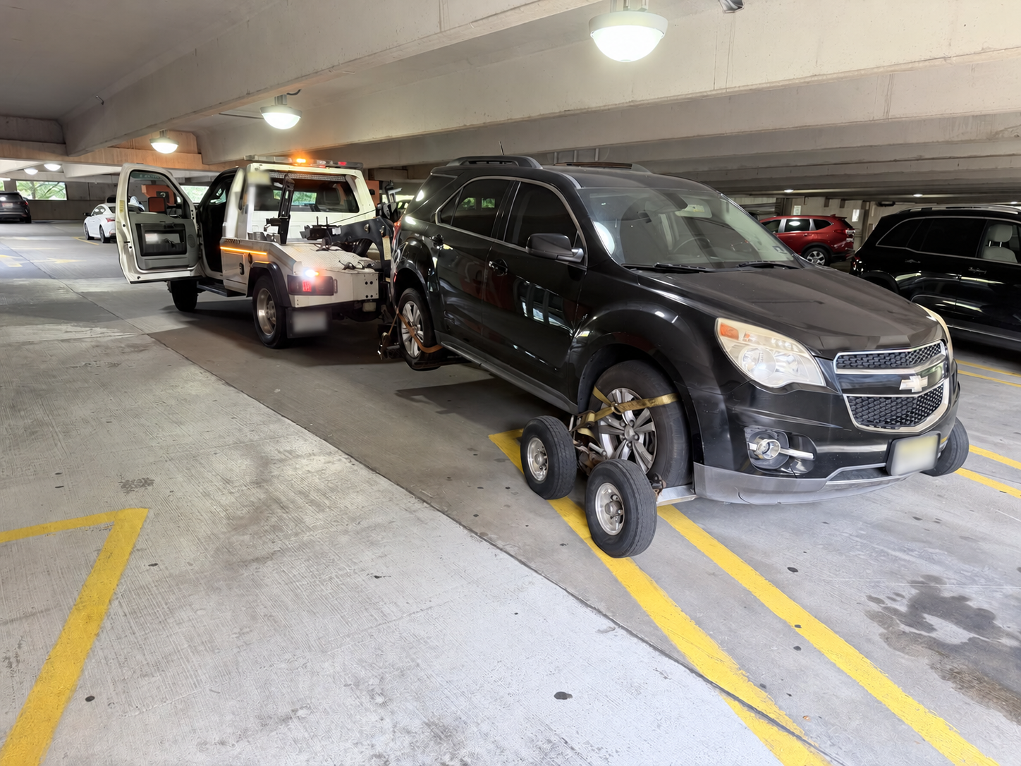 Chevrolet SUV on wheel dollies with a Chain Gang wrecker inside a Somerville parking garage.